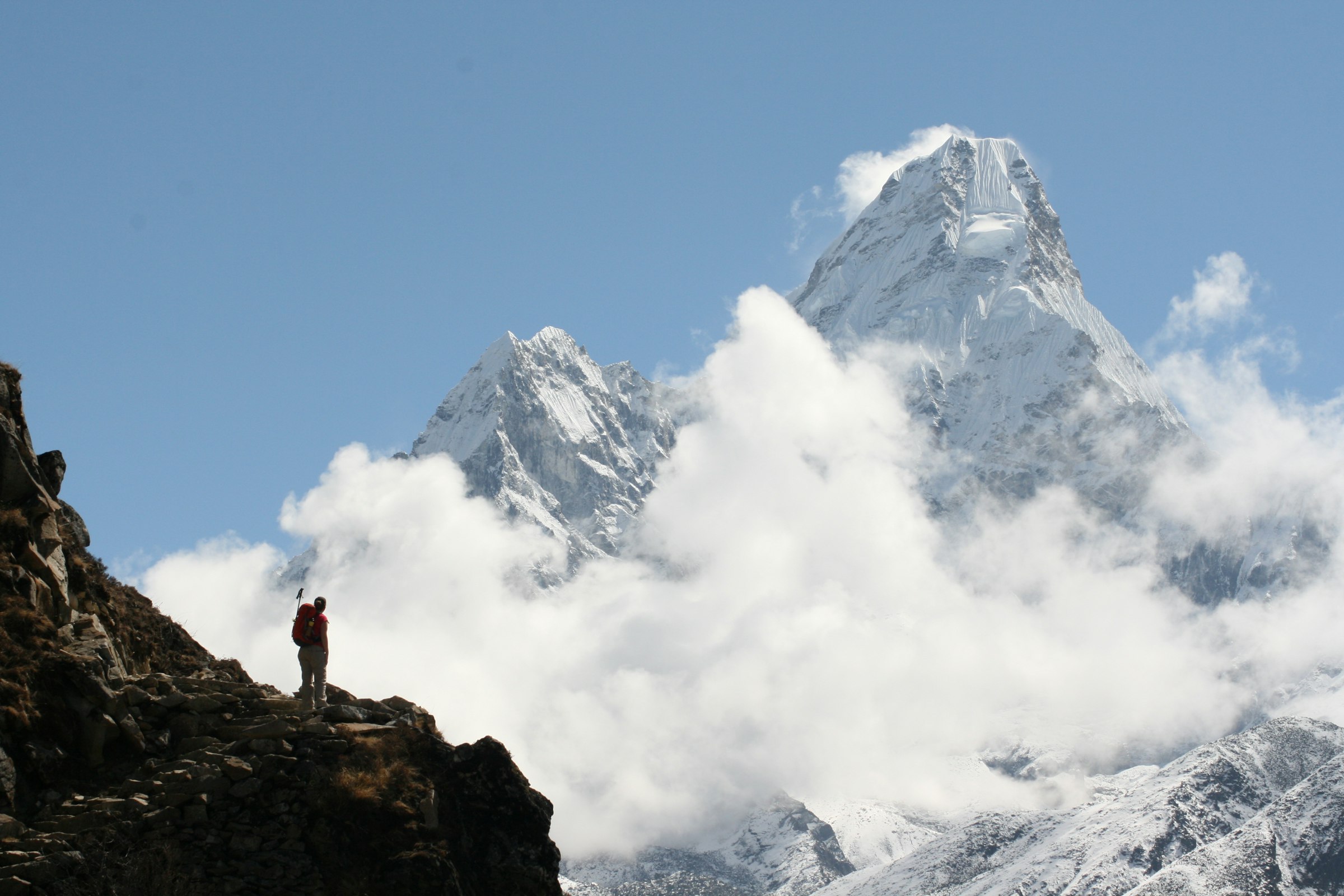 Trekker on a rocky outcrop gazing at Ama Dablam rising above billowing white cloud