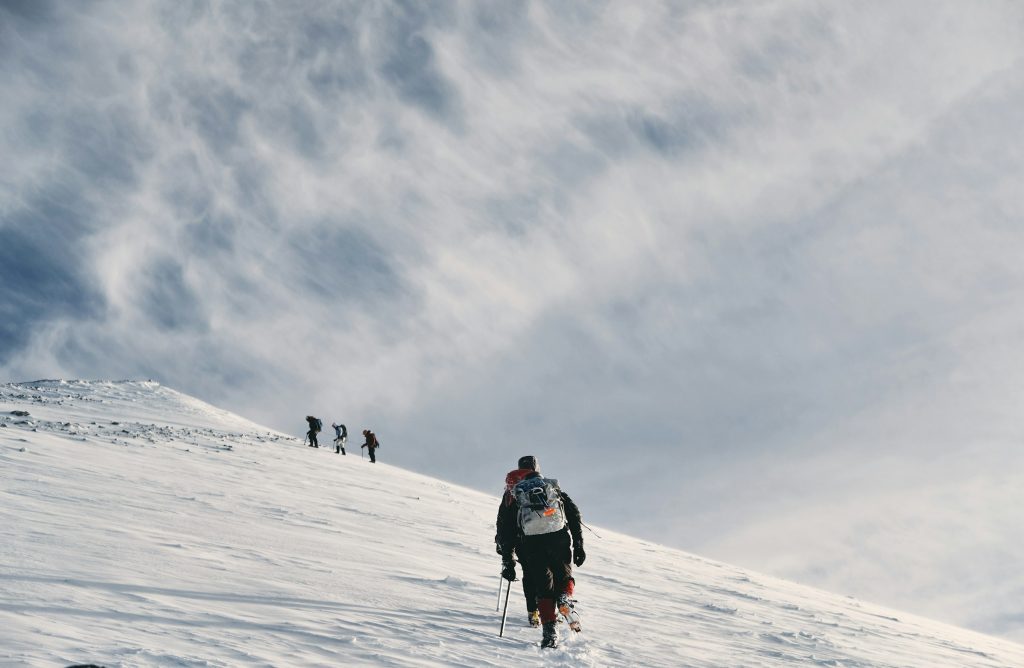 Mountaineers with trekking poles ascending a broad snow slope beneath a streaky cloudy sky