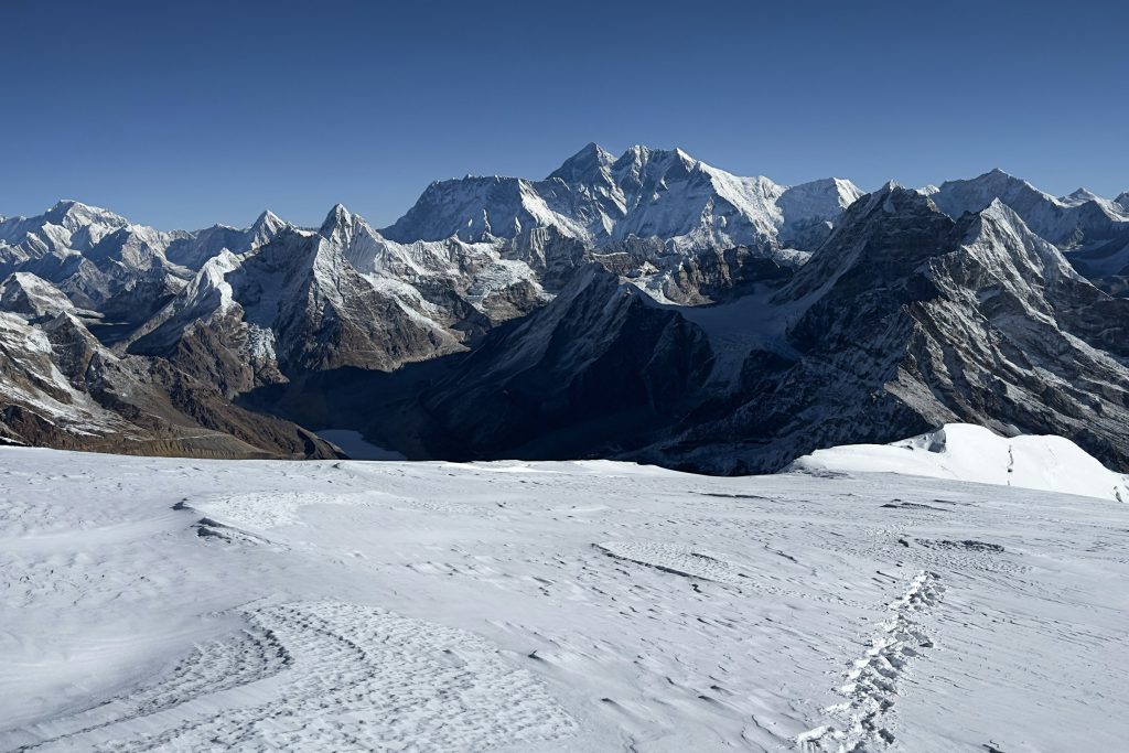 Snowfield with footprints leading towards a panorama of jagged Himalayan peaks under a clear sky
