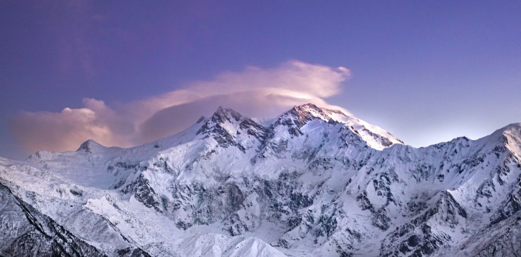 Vast snow-covered mountain massif beneath a pink lenticular cloud at dusk in the Nanga Parbat region