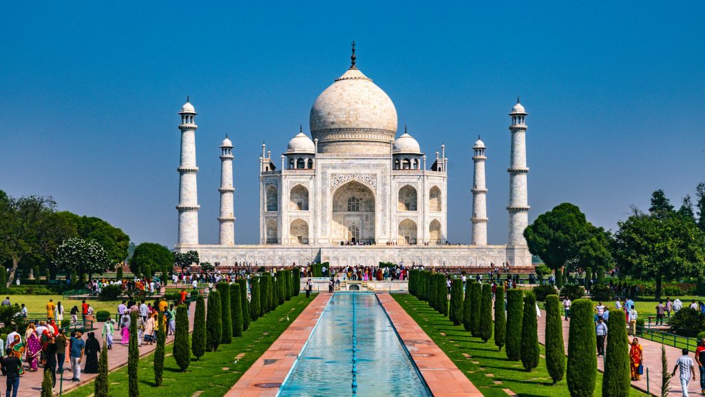 Visitors in the gardens before the Taj Mahal and its long reflecting pool under blue sky