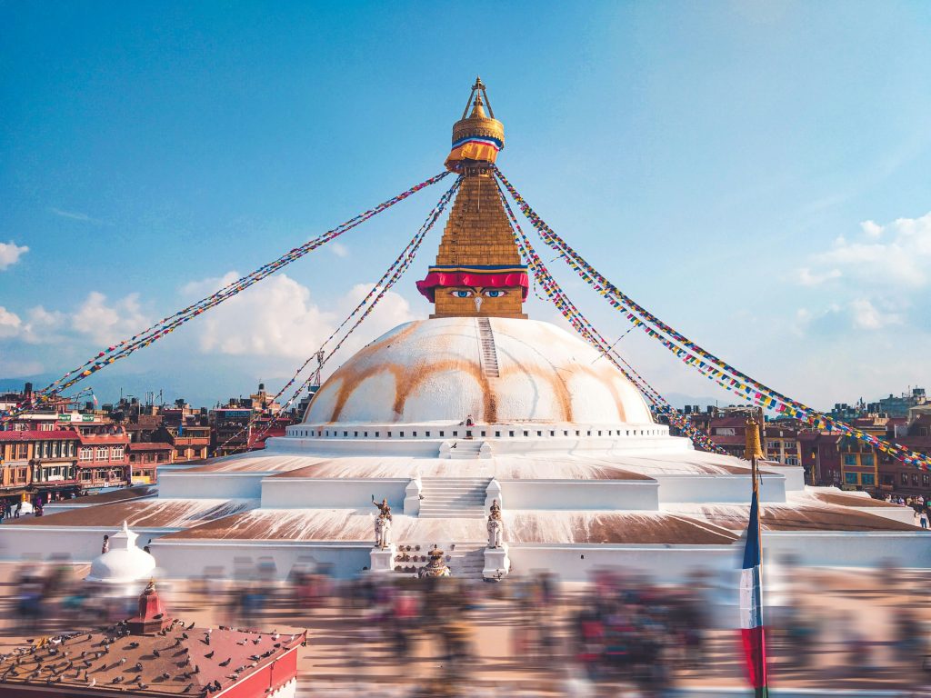 Boudhanath stupa with its golden tower and prayer flags above a motion-blurred crowd of pilgrims