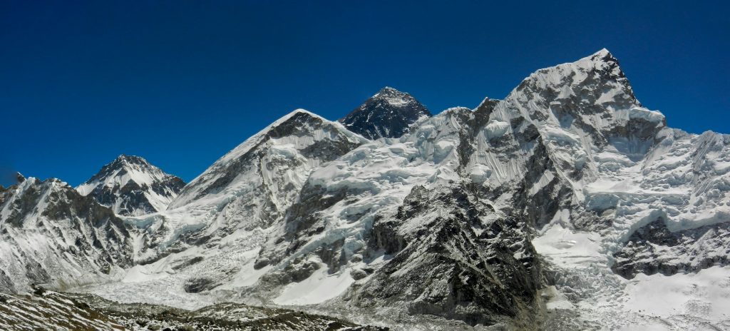 Everest's dark summit behind the snowy ridges of Nuptse above glaciers under a deep blue sky