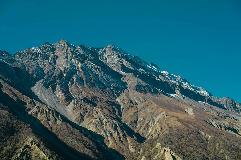 Rugged brown mountainside with eroded gullies and snow on the summit ridge in the Annapurna region