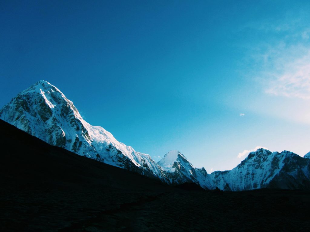 Snowy pyramid peak and ridgeline rising above a shadowed slope against a deep blue sky