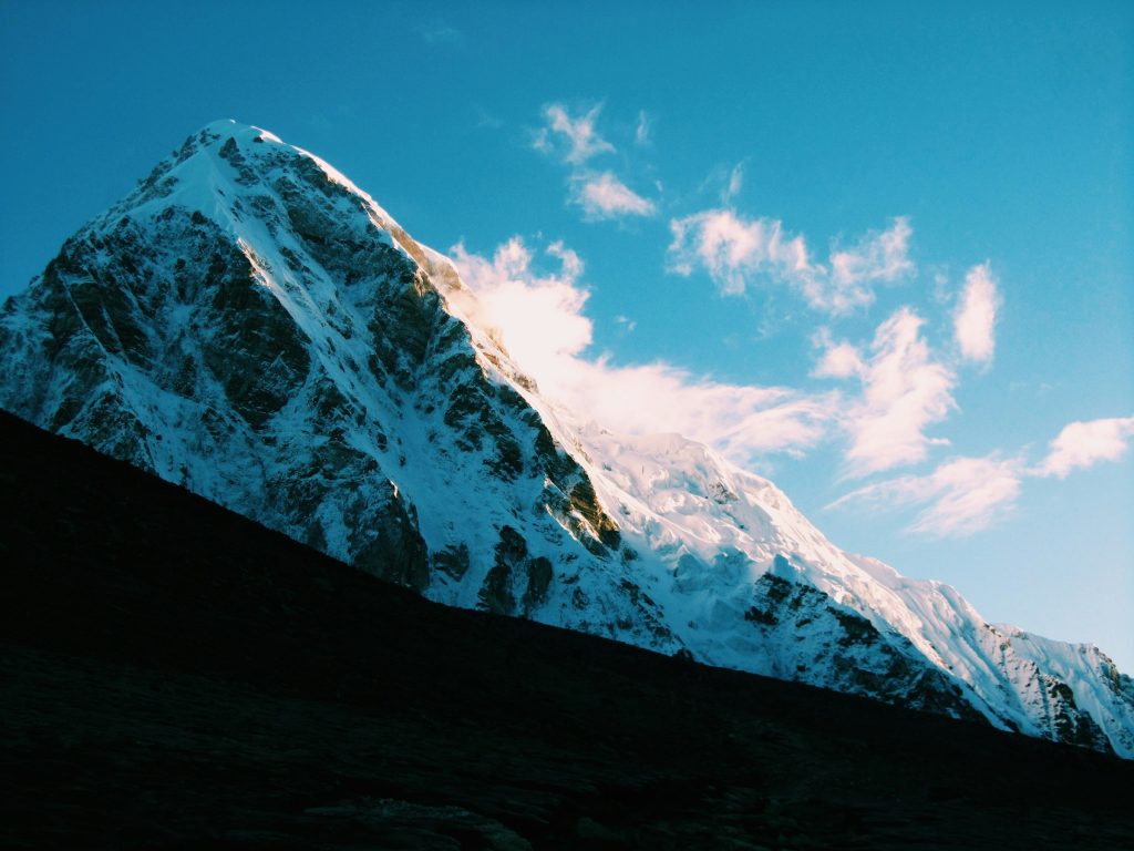 Steep snowy pyramid peak above a dark slope with pink-tinted cloud in the Everest region