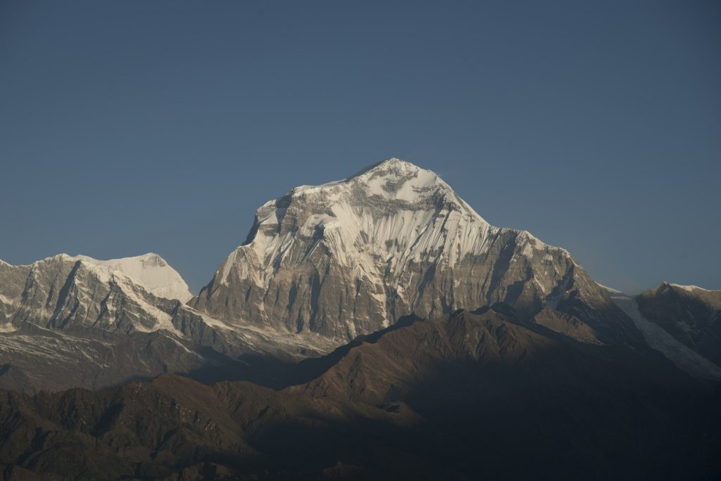 Snow-capped summit lit by soft light above shadowed foothills in the Dhaulagiri region