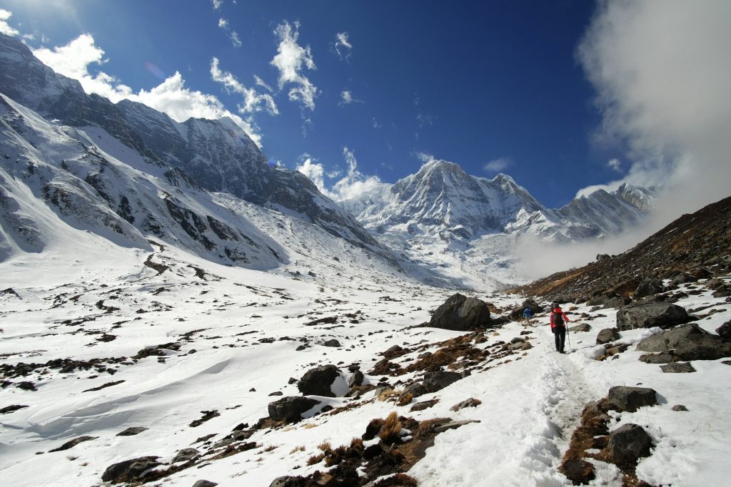 Lone trekker on a snowy trail through a boulder-strewn valley towards snowy peaks in the Annapurna Sanctuary