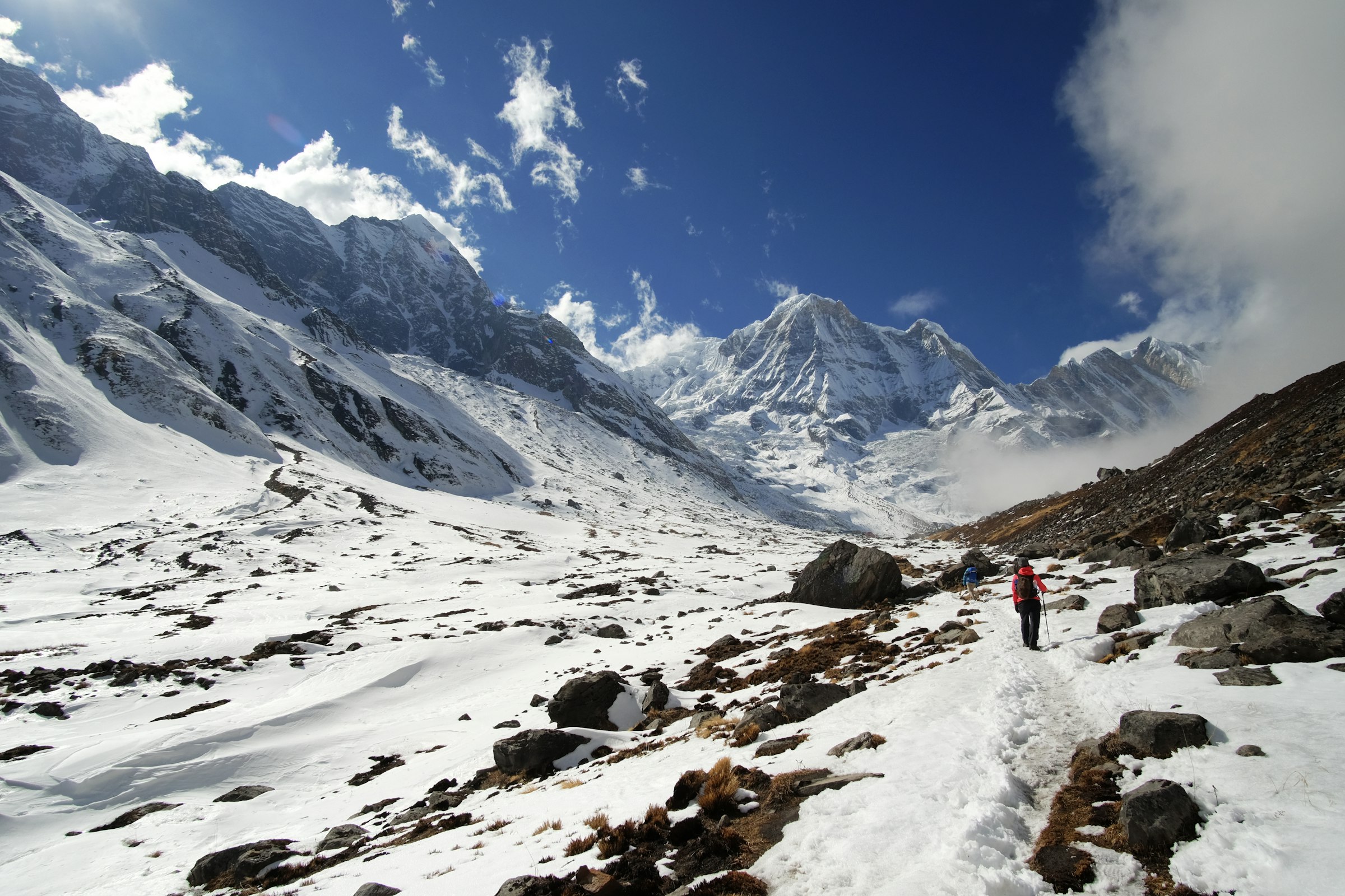 Lone trekker on a snowy trail through a boulder-strewn valley towards snowy peaks in the Annapurna Sanctuary