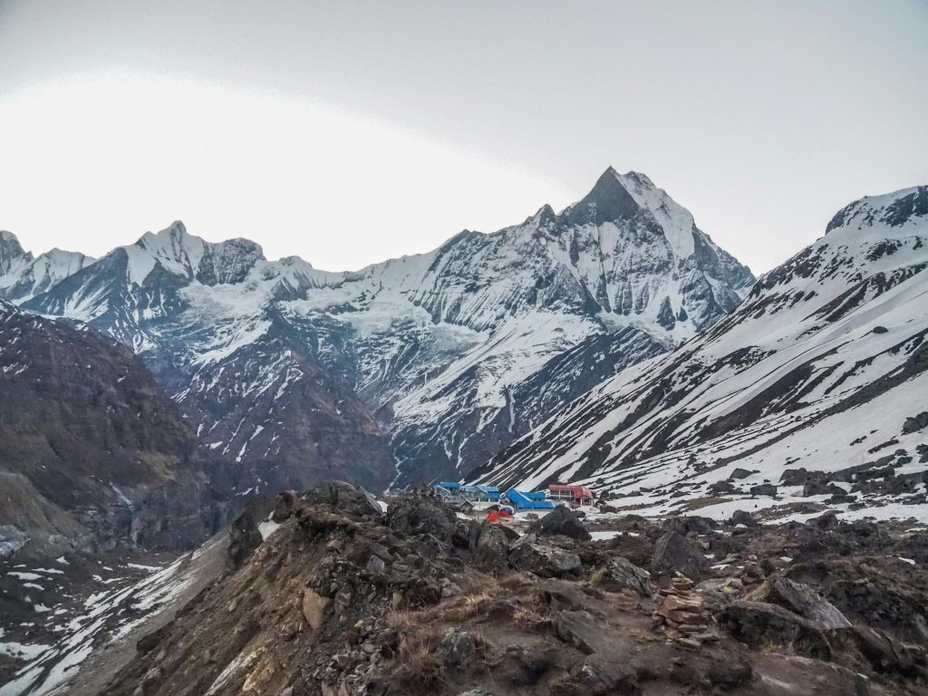 Rocky moraine ridge overlooking blue-roofed lodges with Machhapuchhre's sharp summit rising behind