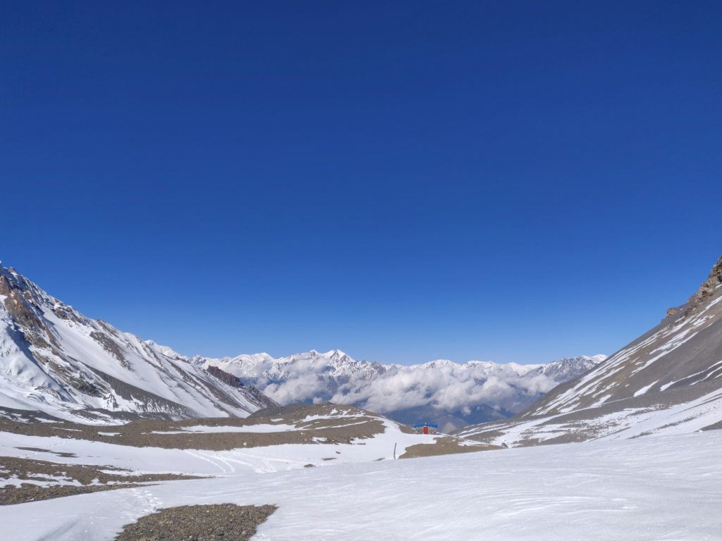 Wide snow-covered pass with distant peaks and cloud under a deep blue sky in the Annapurna region