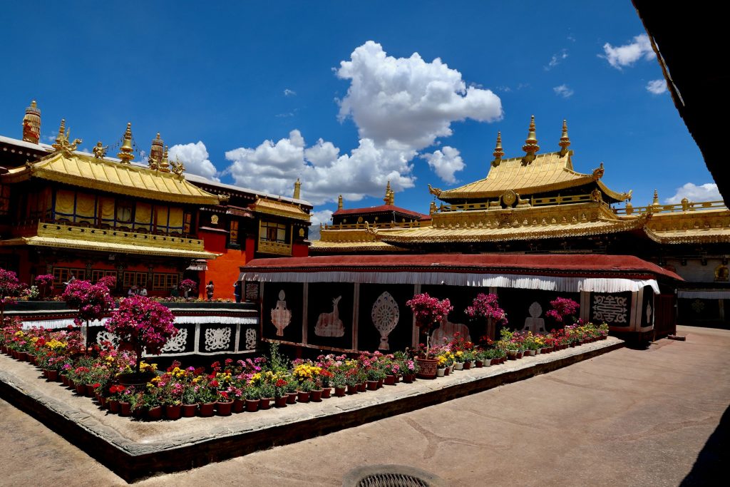 Golden roofs of the Jokhang Temple above a courtyard of pink and red flowers in Lhasa