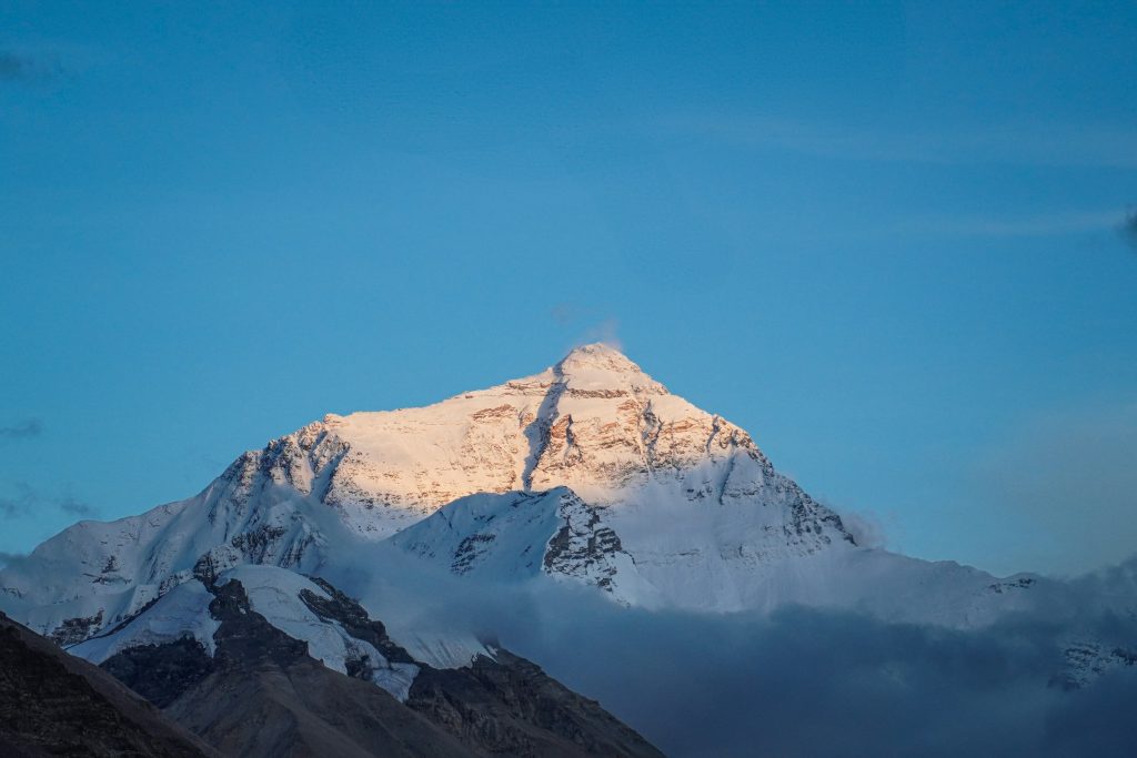 Everest's north face glowing in soft golden light above a band of cloud in Tibet