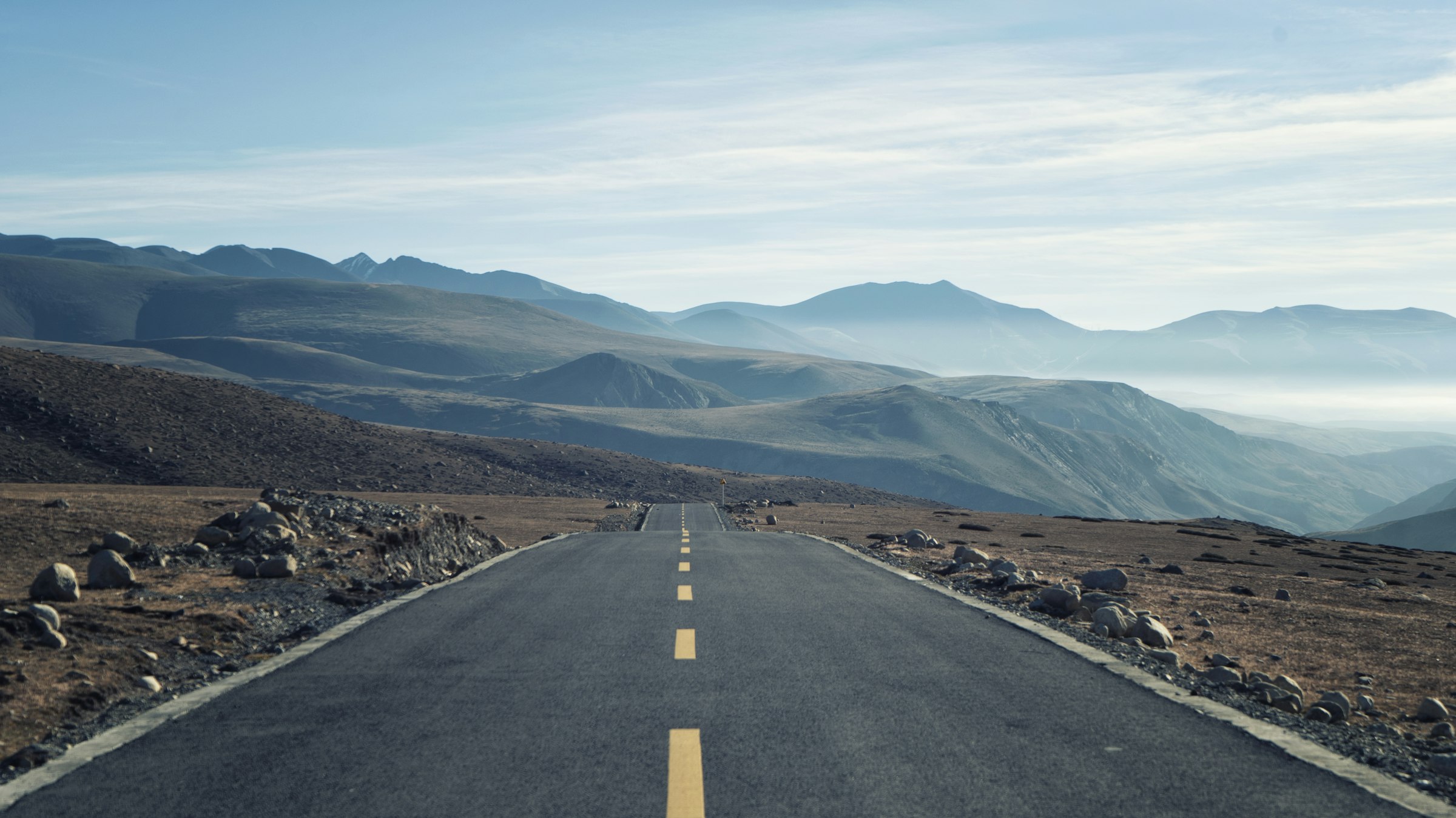 Empty paved road stretching across a barren high plateau towards hazy mountains