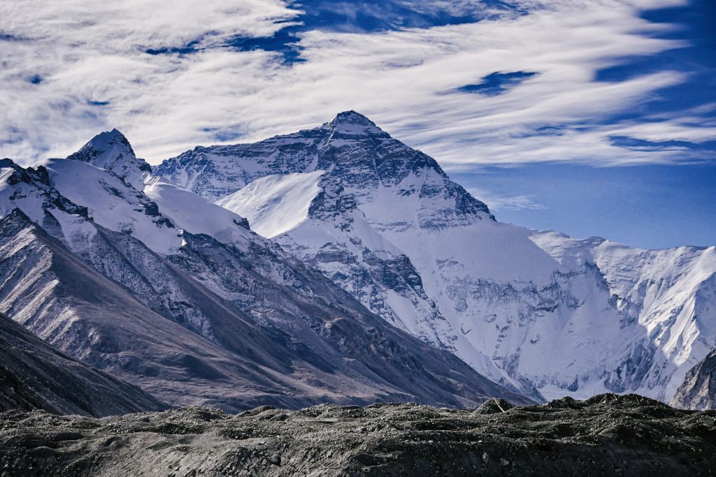 Everest's north face rising above glaciers and rocky ridges under a streaky blue sky in Tibet