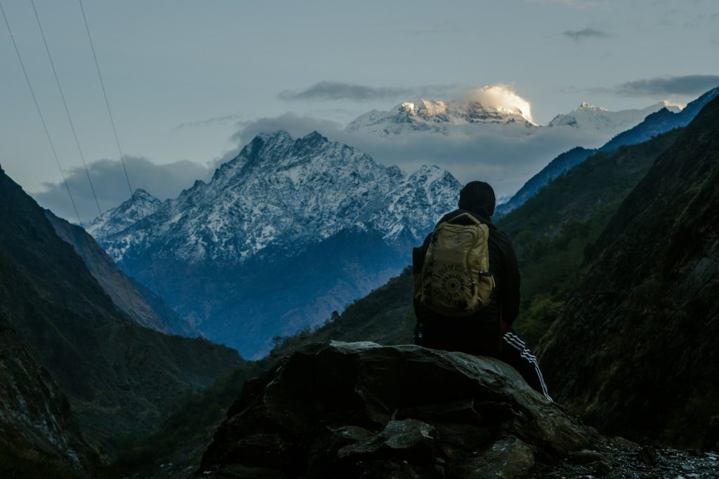 Trekker with a backpack sitting on a rock gazing at a snowy peak across a deep valley