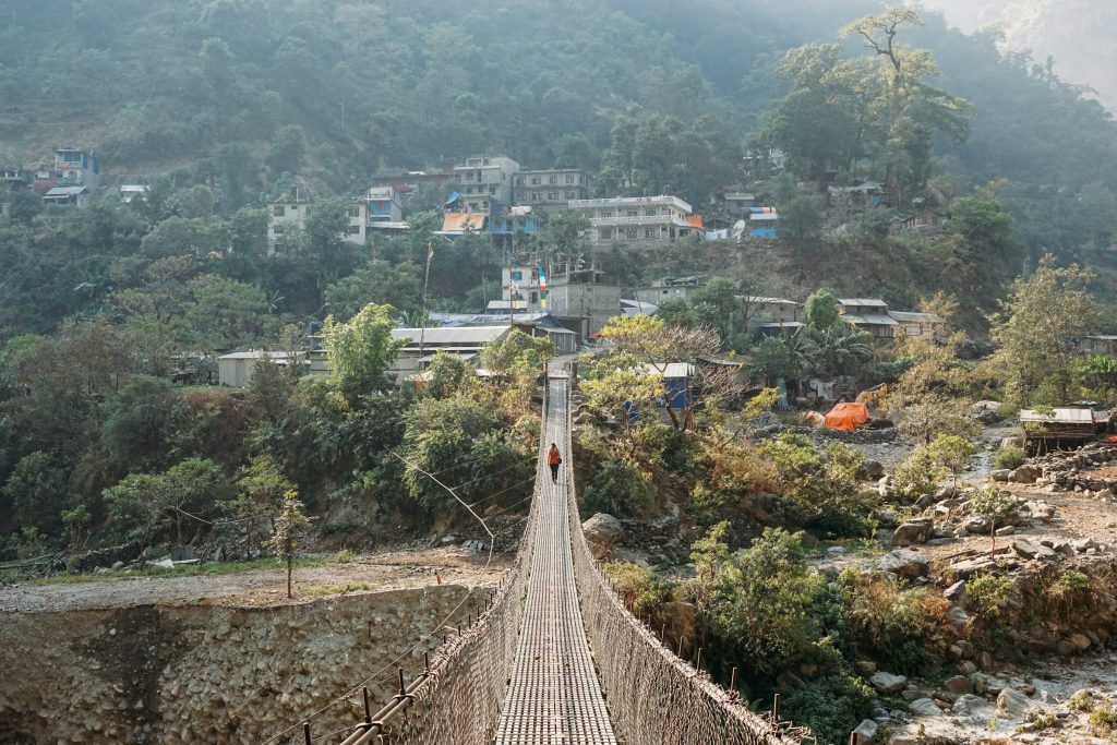 Long steel suspension bridge leading to a riverside village in a forested valley in the Manaslu region