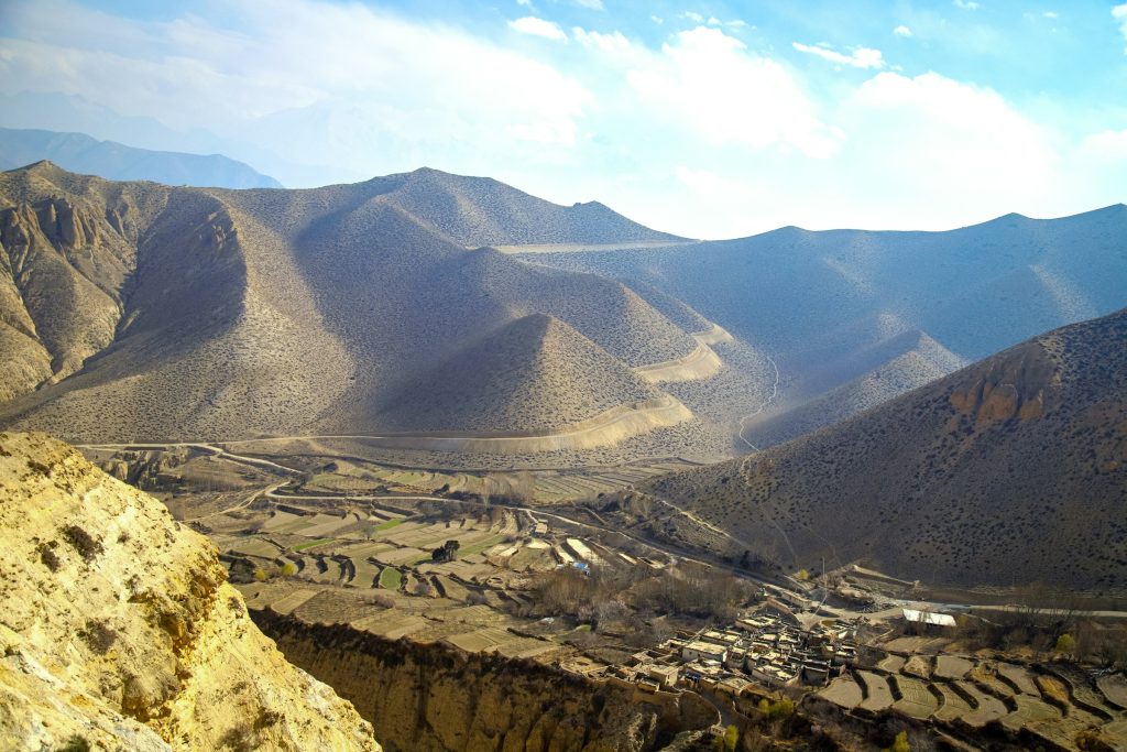 Arid brown hills above terraced fields and a small village in a valley in Upper Mustang