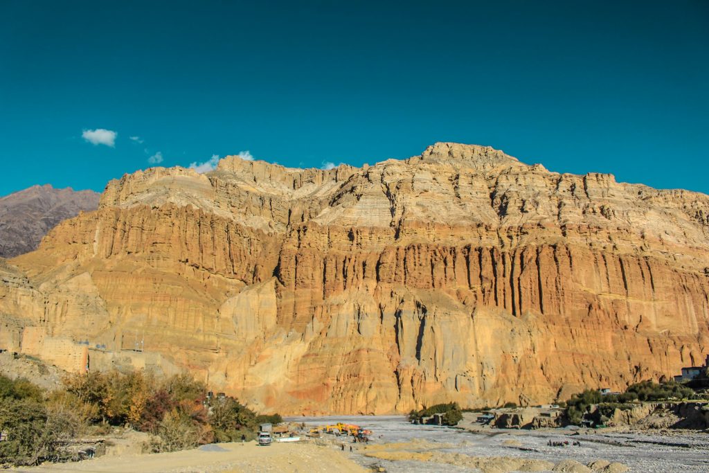 Towering ochre and red eroded cliffs above a dry riverbed under a deep blue sky in Upper Mustang